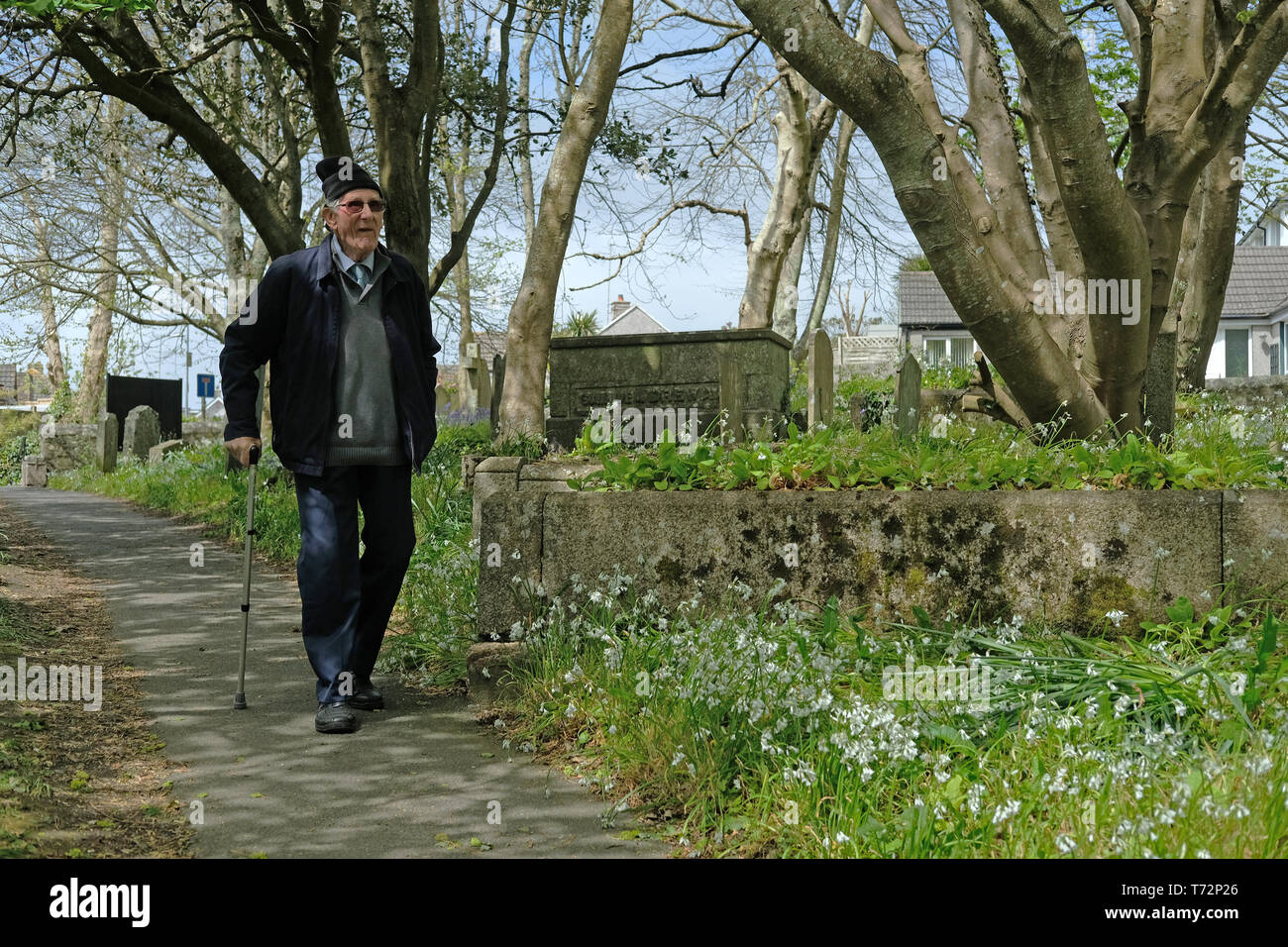 Ein alter Mann zu Fuß durch ein Kirchhof in der Frühlingssonne. Stockfoto