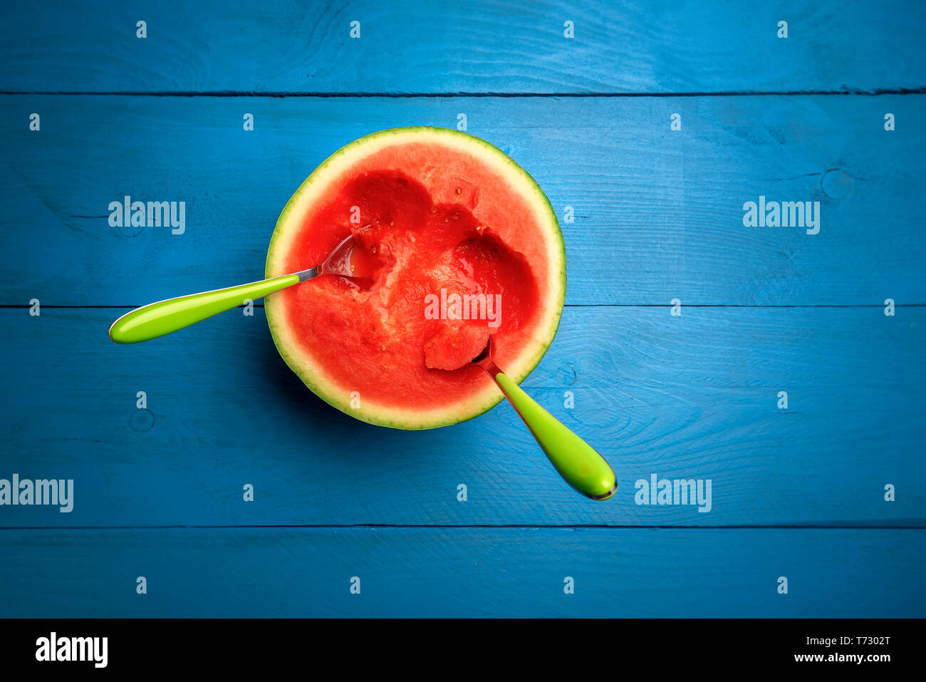 Frische Wassermelone in der Hälfte mit zwei Löffeln in es, auf blauem Hintergrund. Oben Ansicht mit kopieren. Appetitlich aus roten Früchten. Köstliche Sommer behandelt. Stockfoto