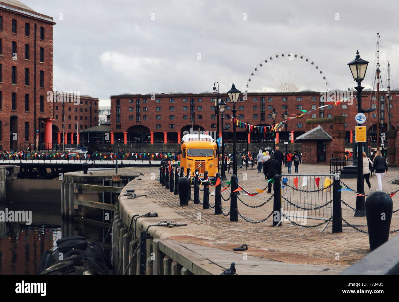Ein gelbes Fahrzeug vor Rot-braune Backsteinhäuser und ein Riesenrad in Liverpool. Stockfoto