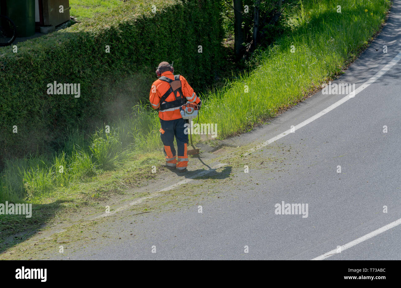 Ein stadtarbeiter Clearing am Straßenrand von Gras und Unkraut mit einem weed Eater Stockfoto