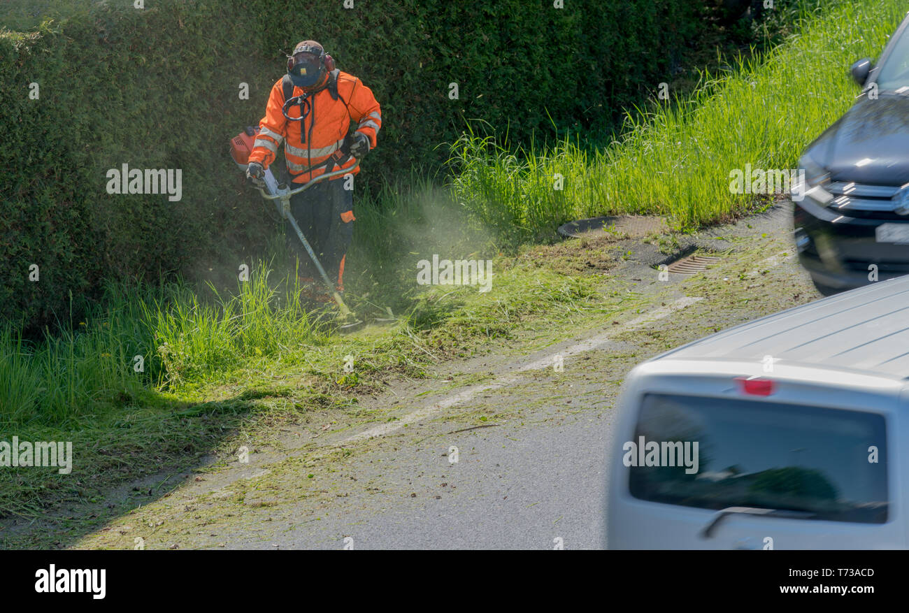 Autos fahren durch ein stadtarbeiter Clearing am Straßenrand von Gras und Unkraut mit einem weed Eater Stockfoto