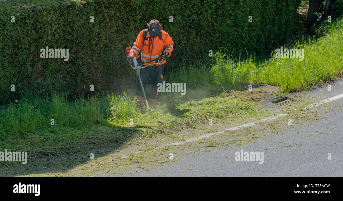 Ein stadtarbeiter Clearing am Straßenrand von Gras und Unkraut mit einem weed Eater Stockfoto