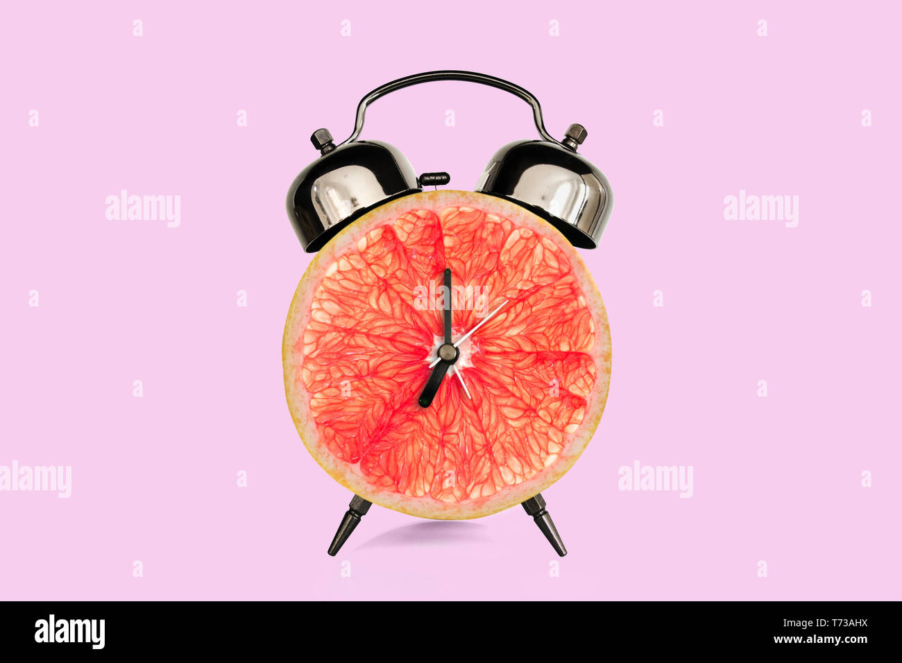 Grapefruit Slice auf Wecker, Rosa pastell Hintergrund. Obst und Vitamine Ernährung beim Frühstück Ernährung Konzept Stockfoto