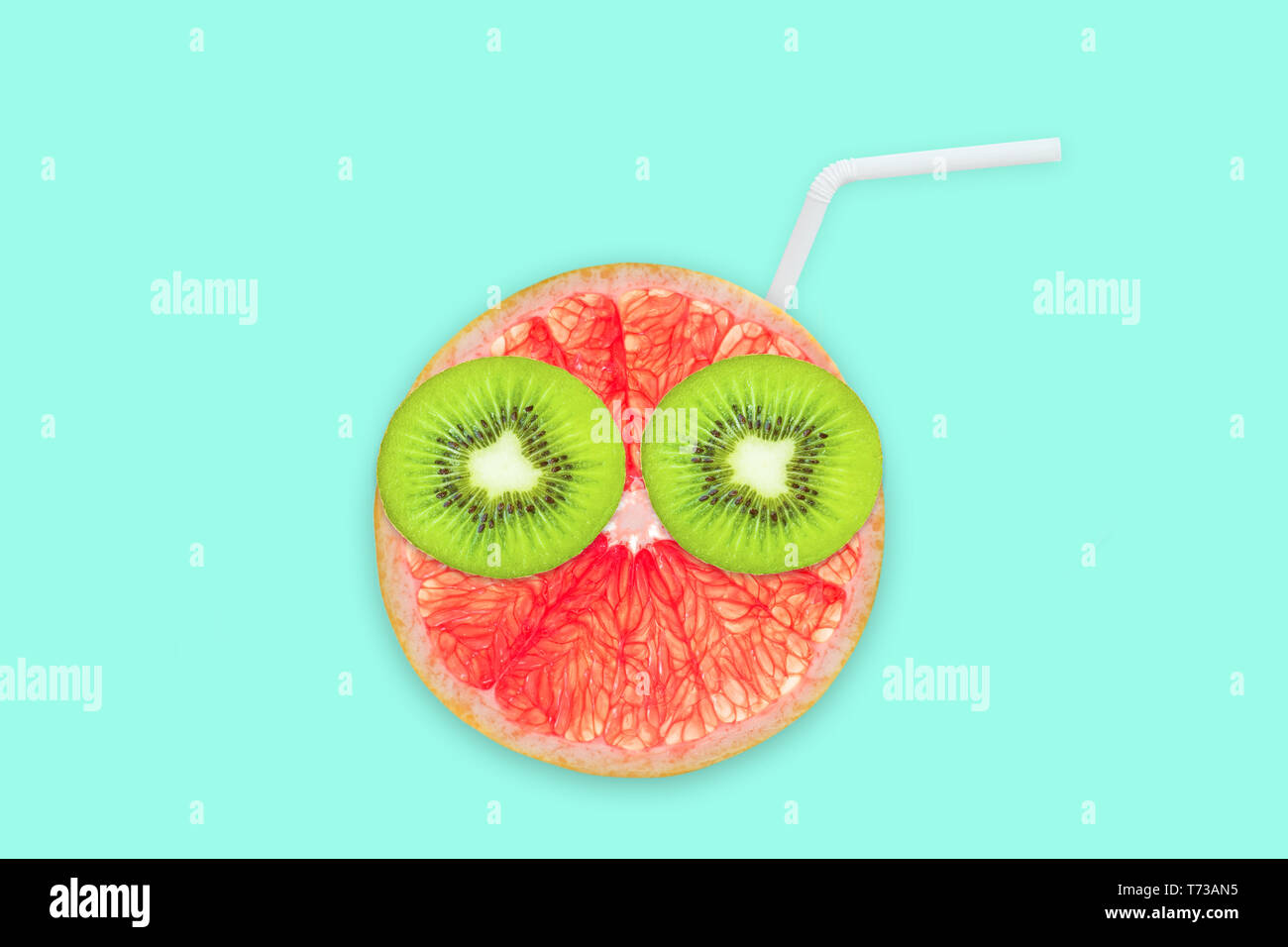 Obst kreative Gesicht mit Scheiben von Grapefruit und Kiwi, Trinkhalm auf blauem Hintergrund, Fruchtsaft und Sommer Konzept Stockfoto