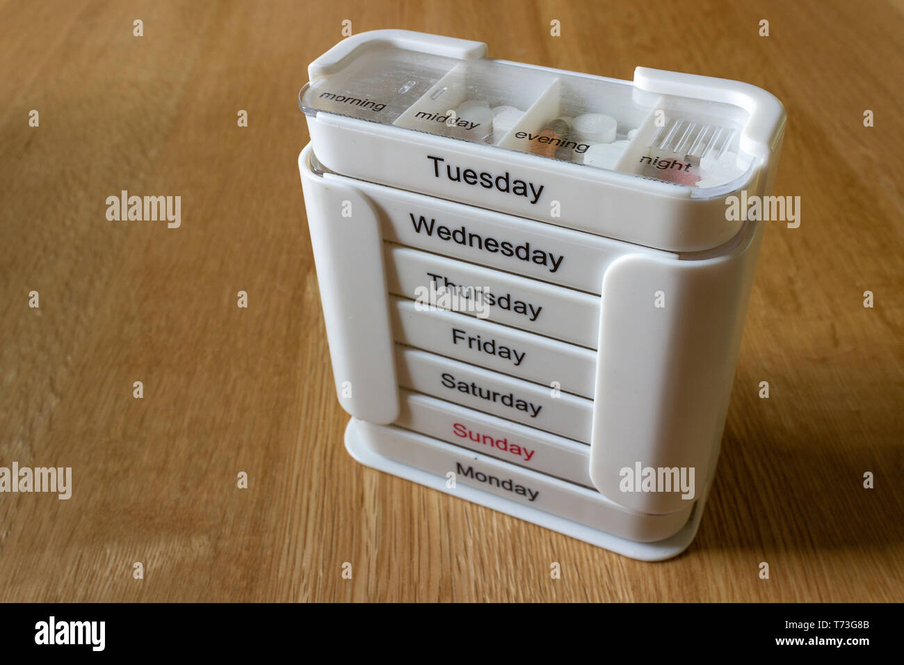 Weiß sieben Tag vier fach Medikamenten Dispenser mit Medikamenten stehen auf einer Eiche Oberfläche. Gegenstand beleuchtet mit natürlichem Licht von Vorne. Stockfoto