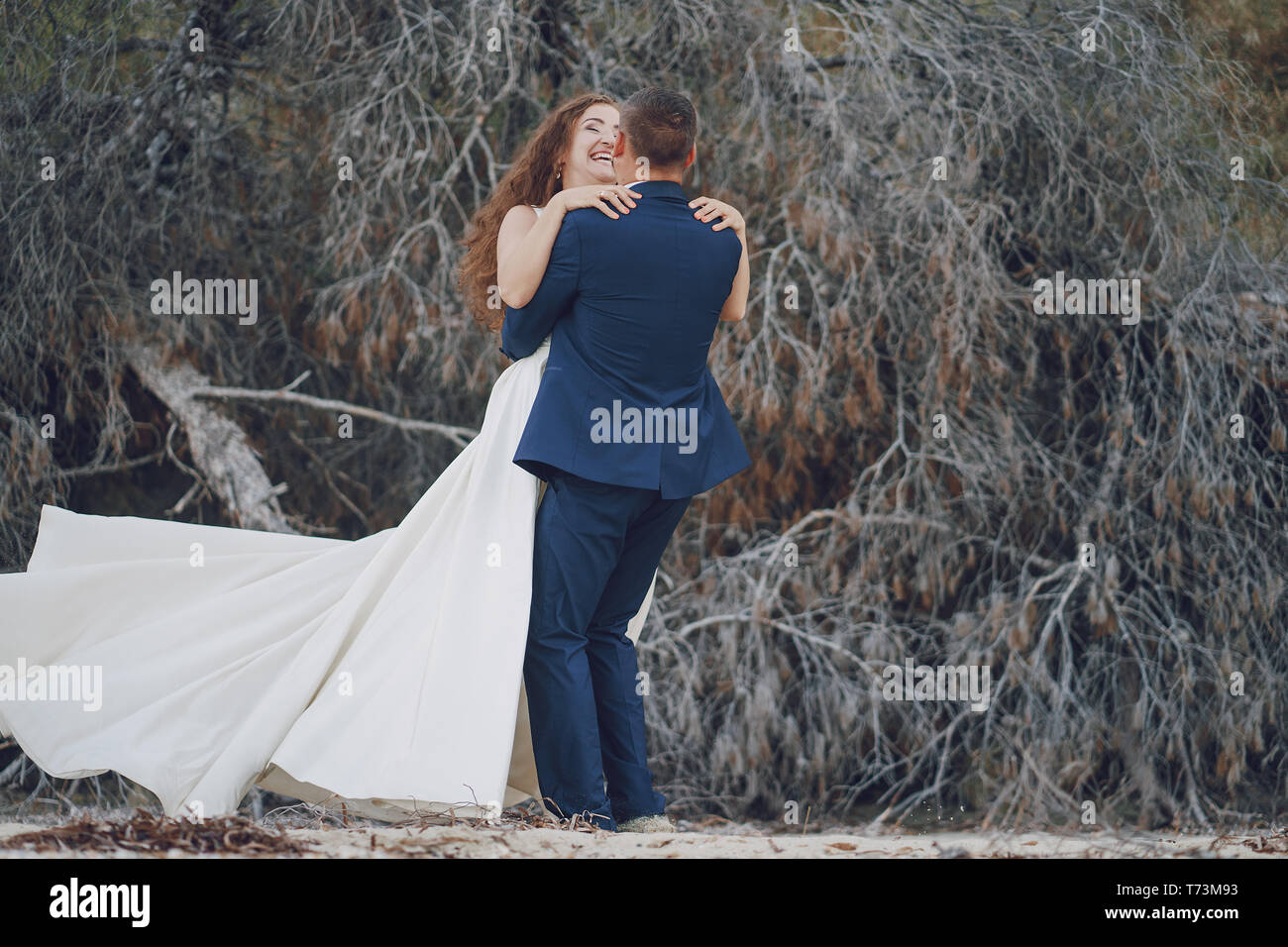 Schönen jungen langhaarigen Braut im weißen Kleid mit ihr junger Ehemann in der Nähe von grau Niederlassungen Stockfoto