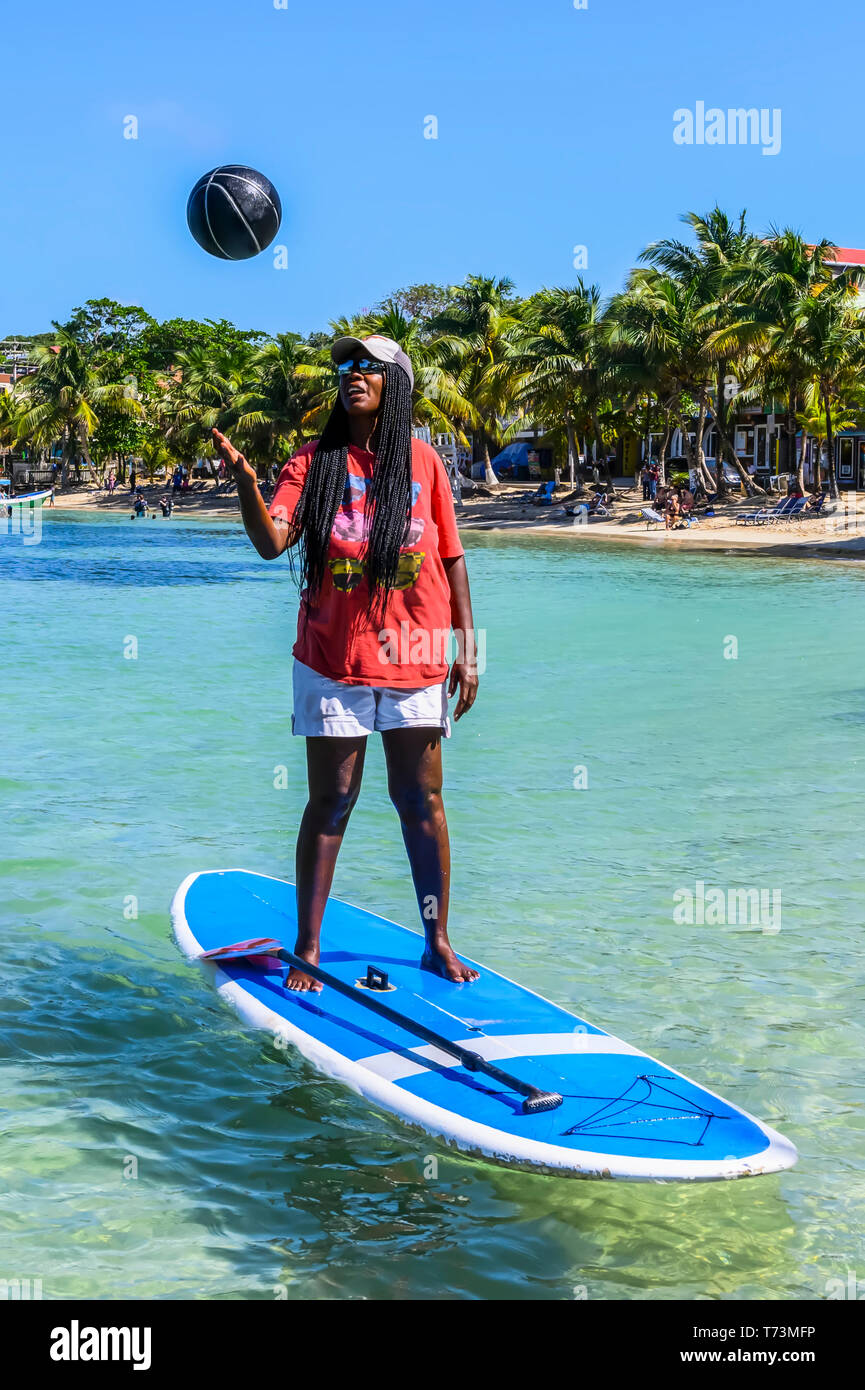 Eine Frau steht ein paddle Board Werfen einer Kugel in der Luft vor der Küste von West End Village; Roatan, Bay Islands, Honduras Stockfoto