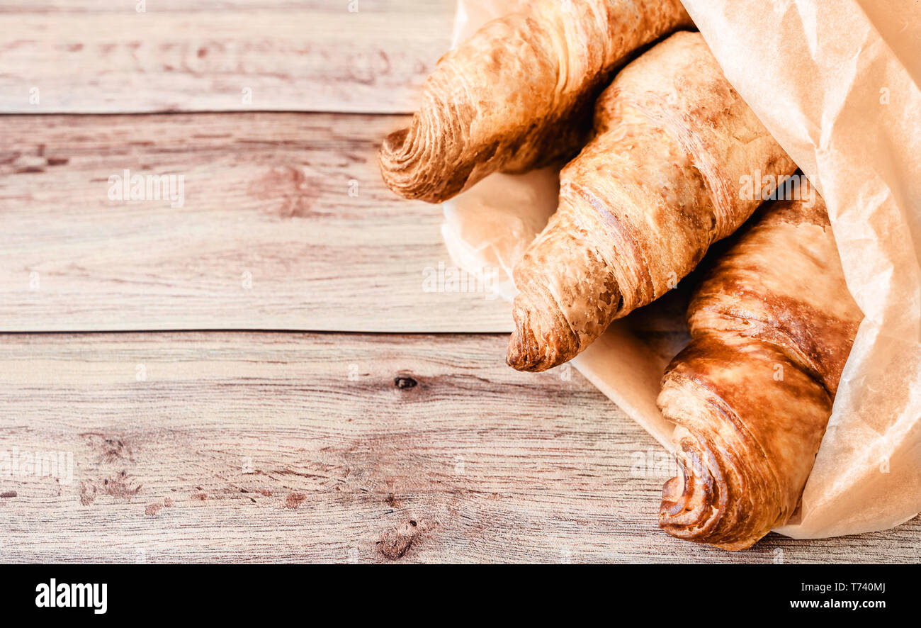 Drei köstliche Croissants in Backpapier auf hölzernen Tisch gewickelt. Ansicht von oben. Kopieren Sie Platz. Stockfoto