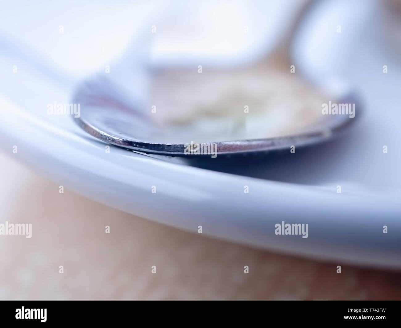 Close-up genau platziert Ort am Rande eines kleinen silbernen Löffel, liegt er auf einer weißen Platte, um leise, leise im Hintergrund. Stockfoto