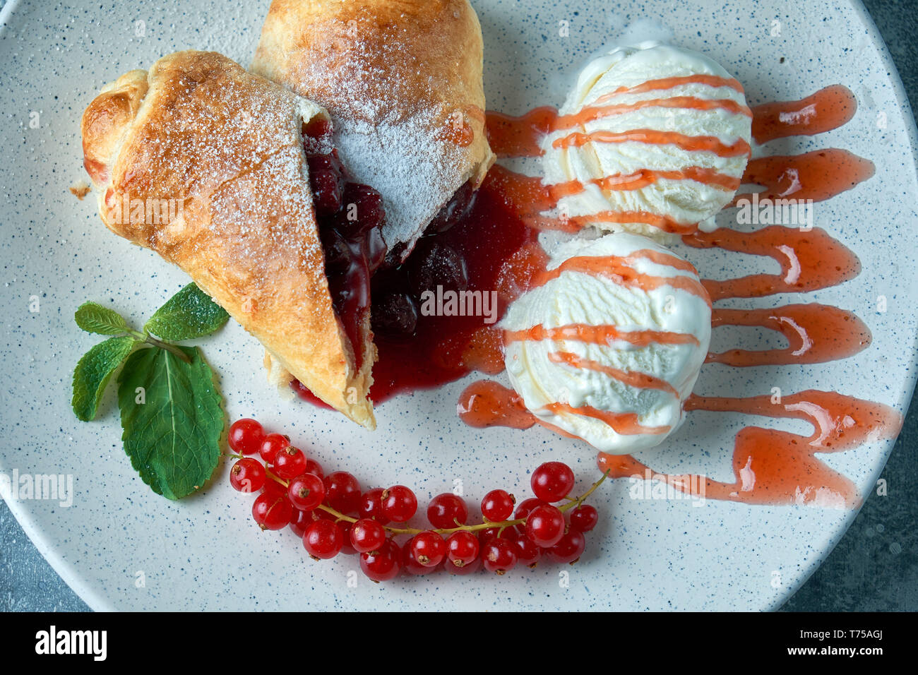 In Scheiben geschnittene Hausgemachte berry Strudel mit frischen rote Johannisbeere Beeren und Puderzucker auf einem alten Hintergrund auf einer Platte mit Eis pic serviert. Stockfoto
