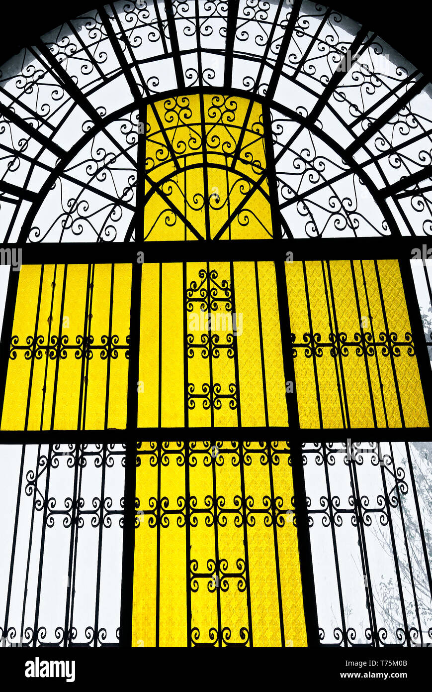 Licht durch eine gelb gefärbte Kreuzes Fenster aus buntem Glas und Metall Werke der Kirche in Leon Stadt scheint, Provinz Iloilo, Philippinen Stockfoto