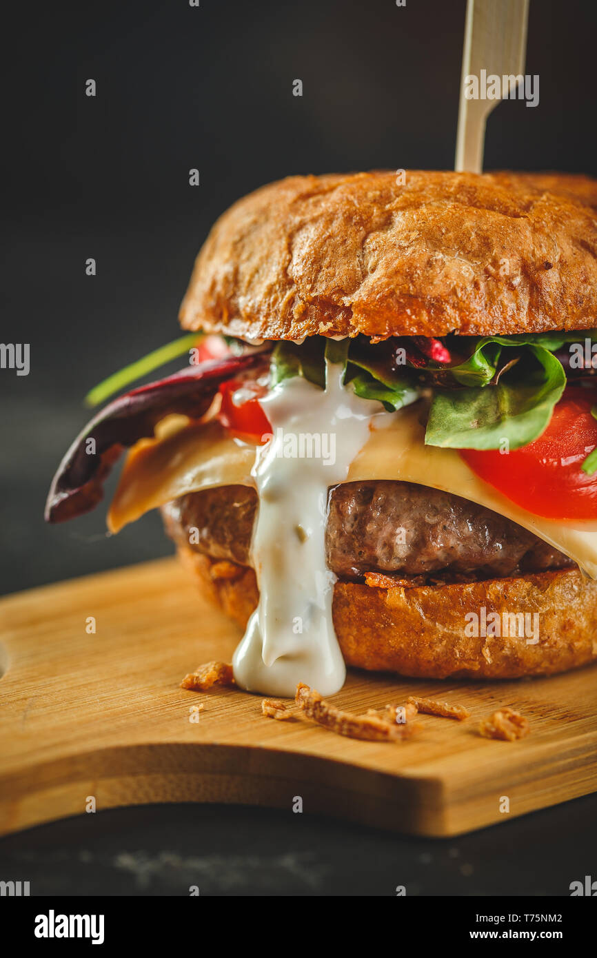 Leckere hausgemachte Burger mit Rindfleisch, Tomaten, Käse, Rucola und Mangold auf einer hölzernen Schneidebrett. Street Food, Fast Food. Stockfoto