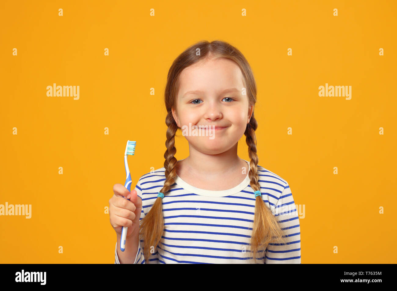 Ein kleines Kind Mädchen in einem gestreiften Pyjama Holding eine Zahnbürste. Das Konzept der täglichen Hygiene. Gelber Hintergrund. Stockfoto