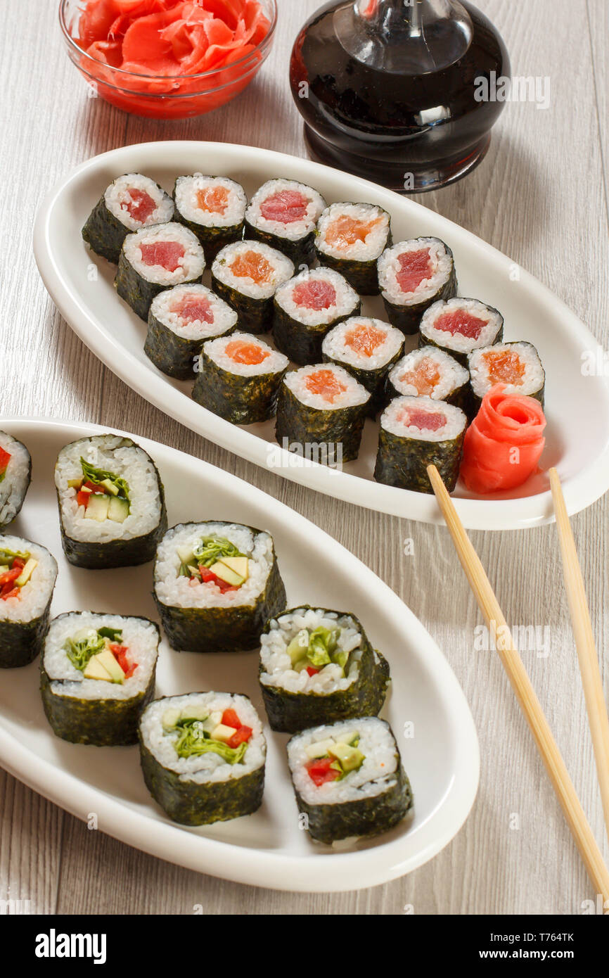 Verschiedene sushi Rollen mit Reis und Algen, Blätter, die auf Keramik Teller, Essstäbchen, Glasflasche mit Sojasauce und eingelegtem Ingwer in eine Schüssel geben. Ansicht von oben. Stockfoto