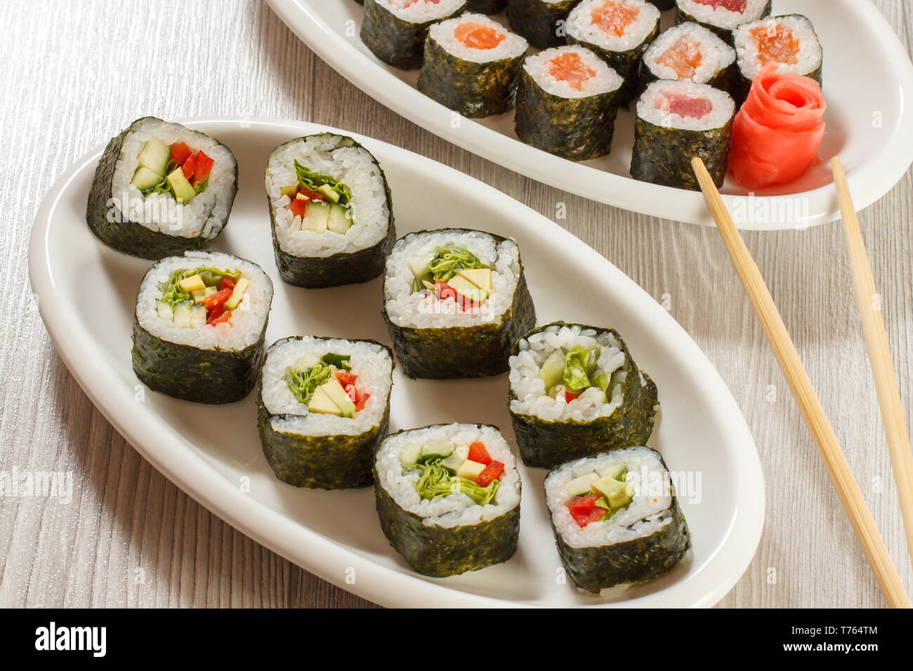 Verschiedene sushi Rollen mit Reis und Algen, Blätter, die auf Keramik Teller, Essstäbchen und eingelegter Ingwer. Ansicht von oben. Stockfoto