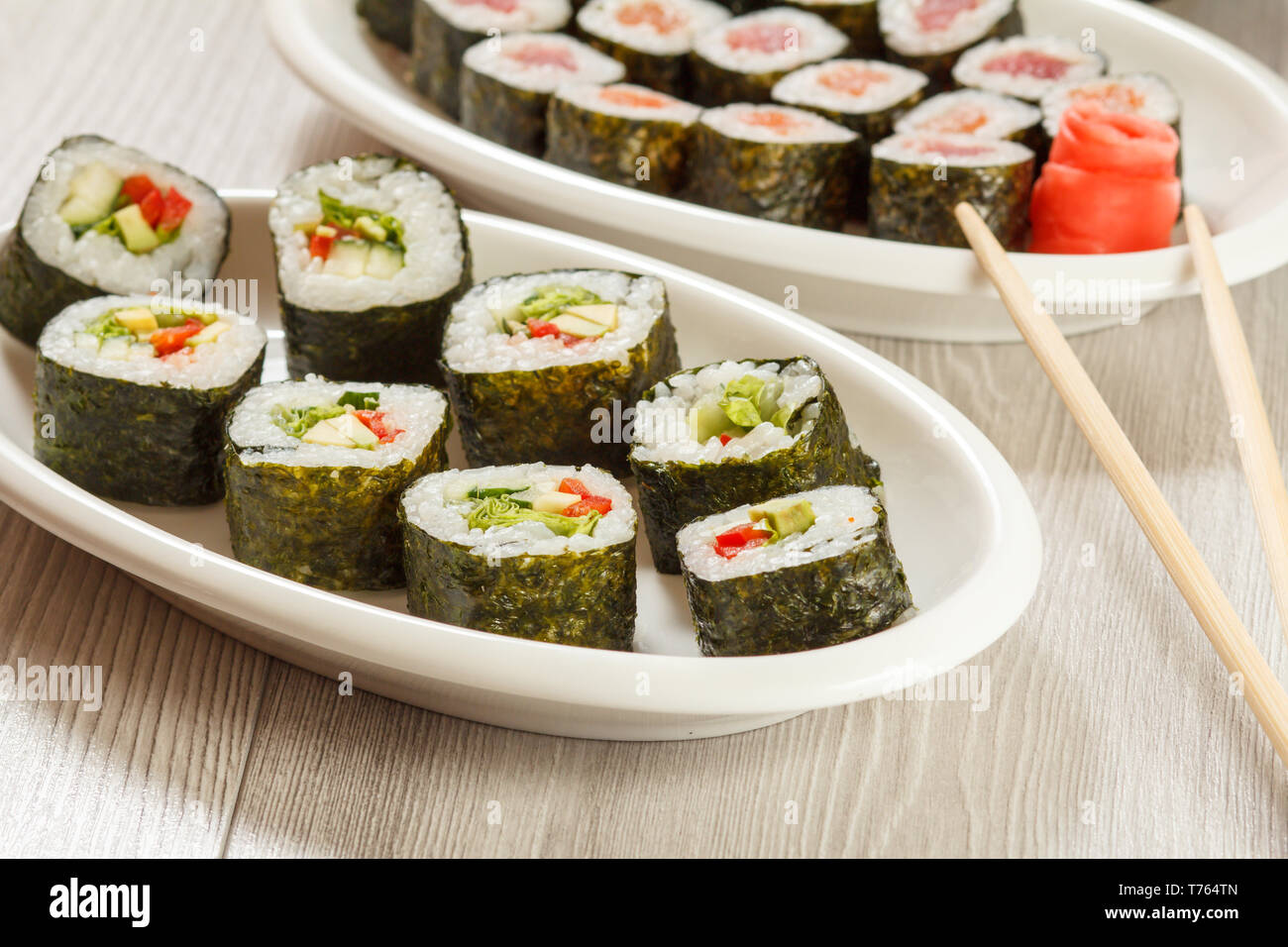 Verschiedene sushi Rollen mit Reis und Algen, Blätter, die auf Keramik Teller, Essstäbchen und eingelegter Ingwer. Ansicht von oben. Stockfoto