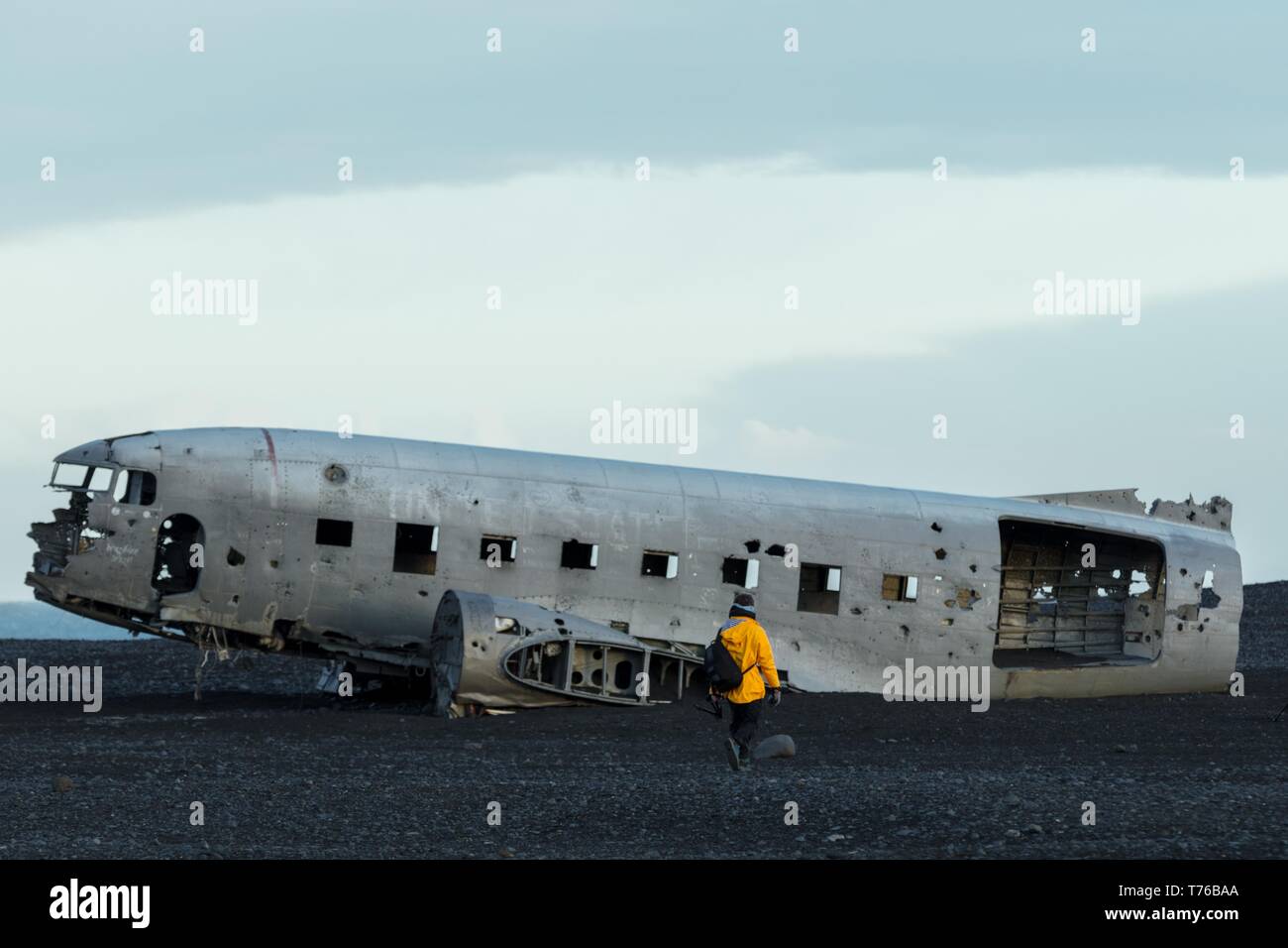 Eine Person in einem gelben Regenmantel, die sich einem alten näherte, stürzte ab Flugzeug in einem Feld Stockfoto
