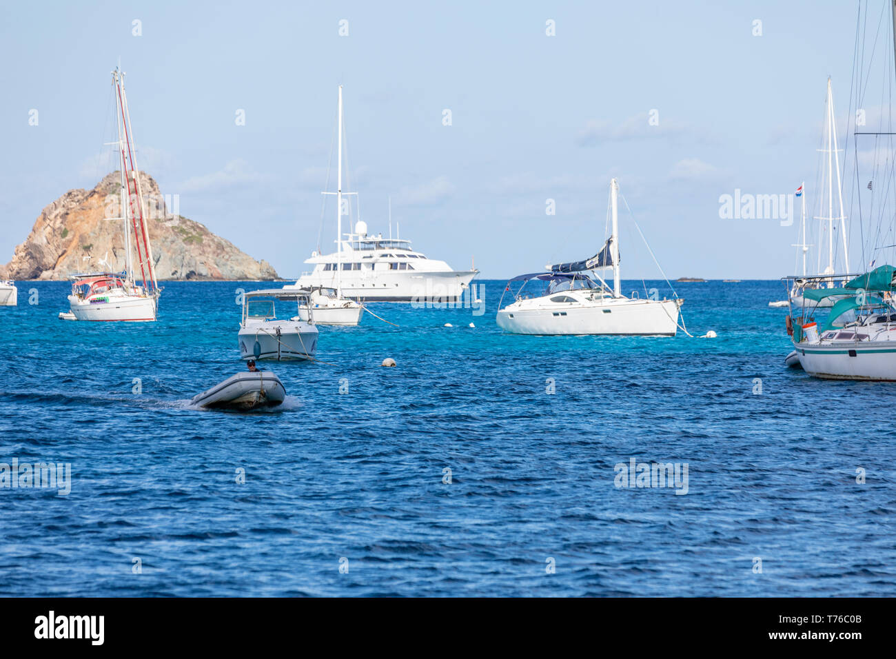 Eine Person, die ein kleines Beiboot in der Nähe der größeren Boote in den Hafen von Gustavia in St. Barts Stockfoto
