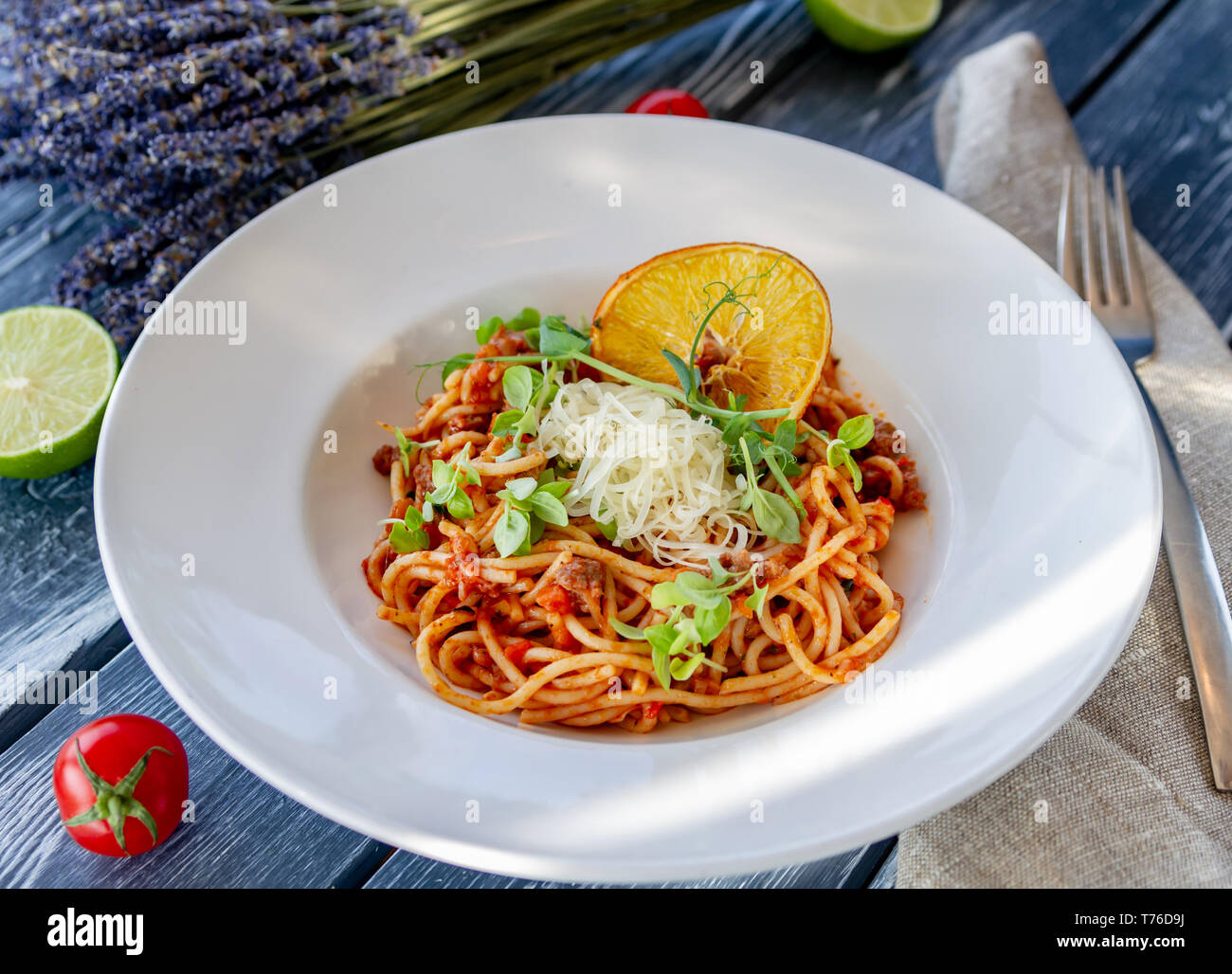 Klassische italienische Pasta Bolognese, mit microgreen, geriebenem Parmesan und einem Stück trockenen Orange auf einem Tisch an einem sonnigen Tag eingerichtet, auf einem Tisch mit Tom Stockfoto