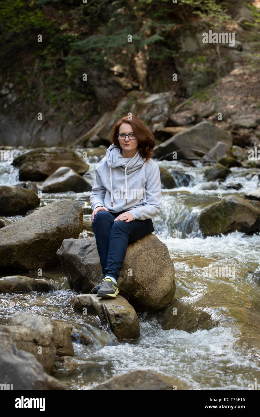 Junge Frau sitzt auf einem Felsen in der Mitte des Flusses Stockfoto