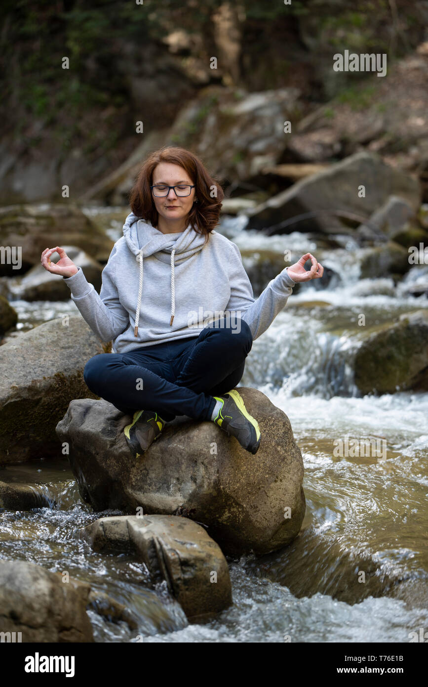 Junge Frau Yoga zen auf einem Felsen in der Mitte des Flusses in einem Wald Stockfoto