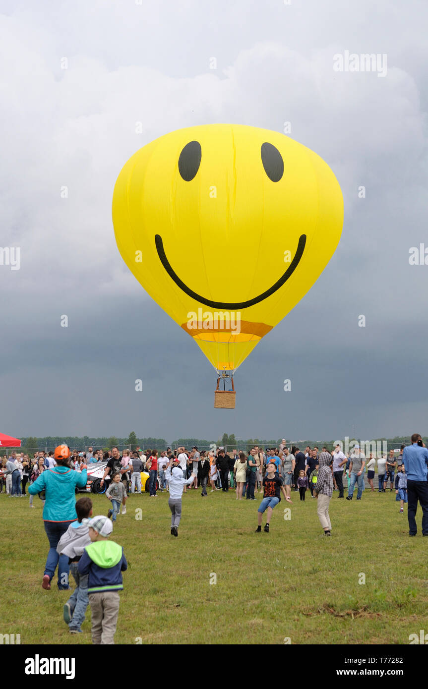 Gelber Ballon mit dem Smiley-Gesichts-Symbol, der über dem Feld fliegt, eine Menschenmenge versammelte sich und beobachtete. 7. Flugshow. Juni 21,2018. Kiew, Ukraine Stockfoto
