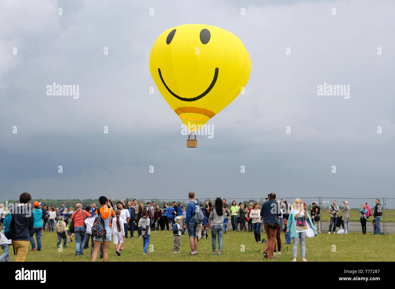 Gelber Ballon mit dem Smiley-Gesichts-Symbol, der über dem Feld fliegt, eine Menschenmenge versammelte sich und beobachtete. 7. Flugshow. Juni 21,2018. Kiew, Ukraine Stockfoto