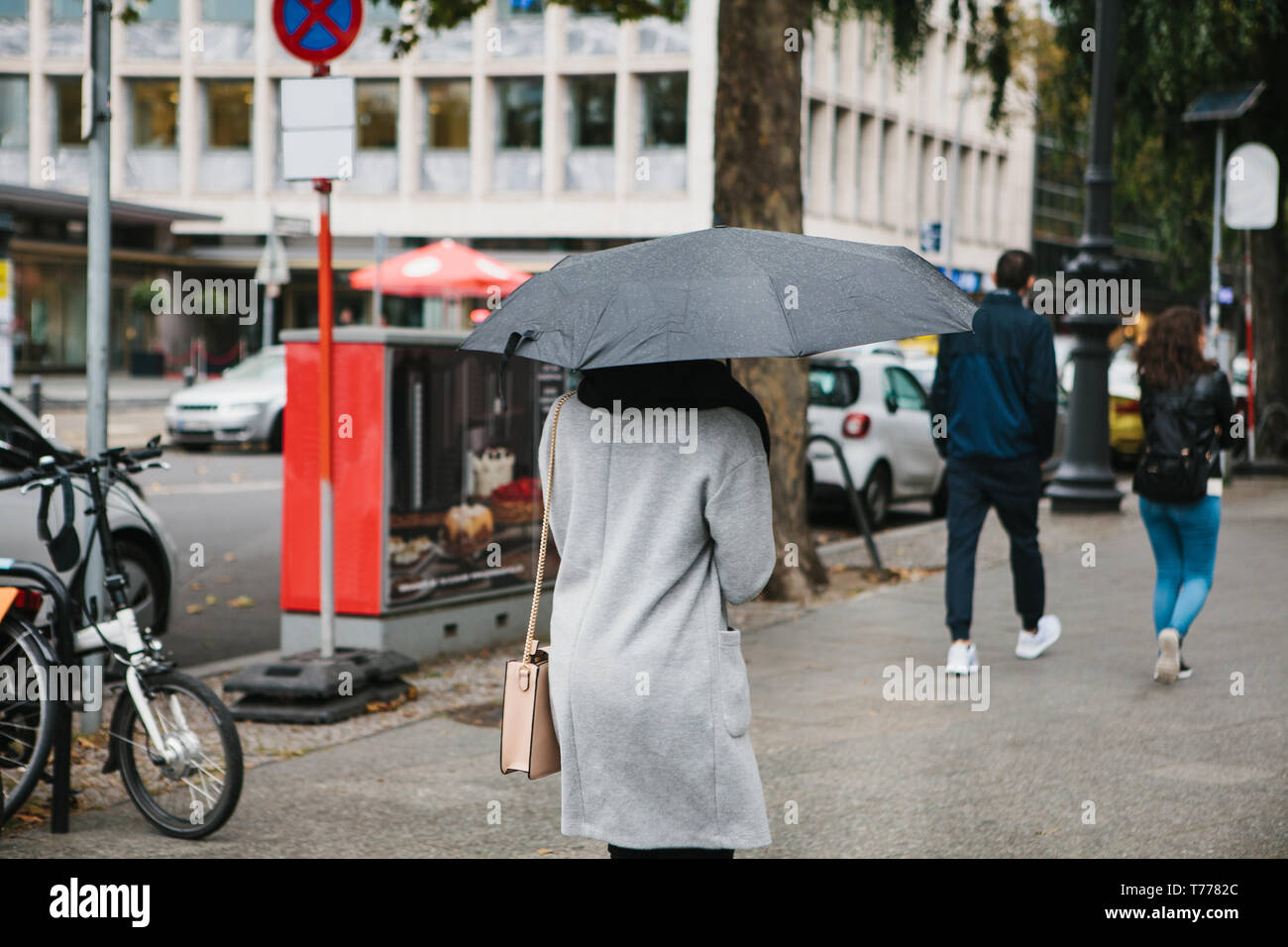 Eine Frau mit einem Regenschirm ist zu Fuß entlang der Straße von Berlin in Deutschland bei Regenwetter. Stockfoto