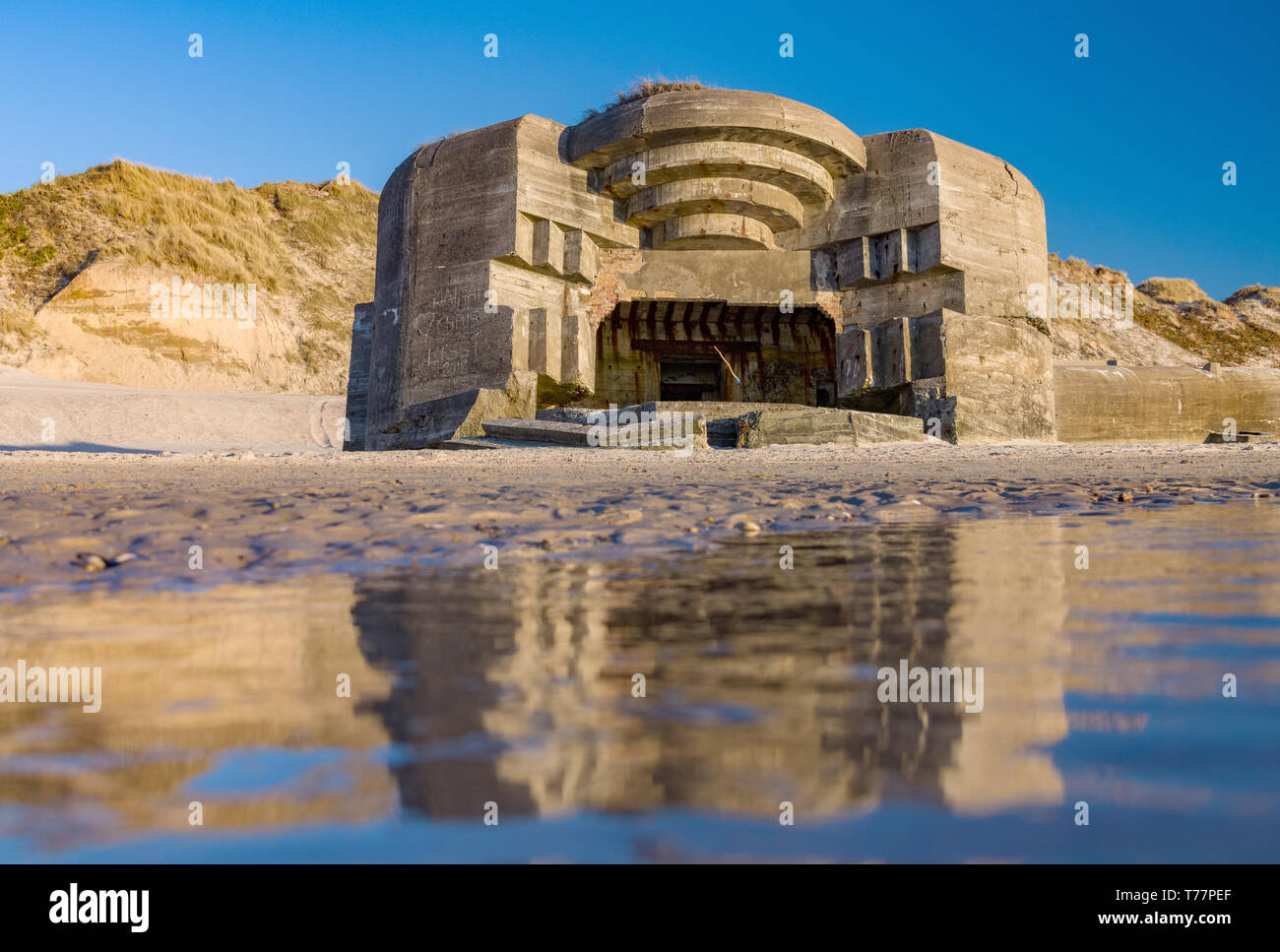 22. April 2019, Dänemark, Lökken: einem deutschen Bunker aus dem Zweiten Weltkrieg am Strand an der Westküste in der Nähe der Ferienort im glatten Wasser der Nordsee wider. Der Bunker ist Teil eines Komplexes von 50 Bunkern und 50 andere Beton und Holz- gebäude, die Teil des "Atlantikwalls" in den Jahren 1943 und 1944 gebaut wurden. Foto: Patrick Pleul/dpa-Zentralbild/ZB Stockfoto