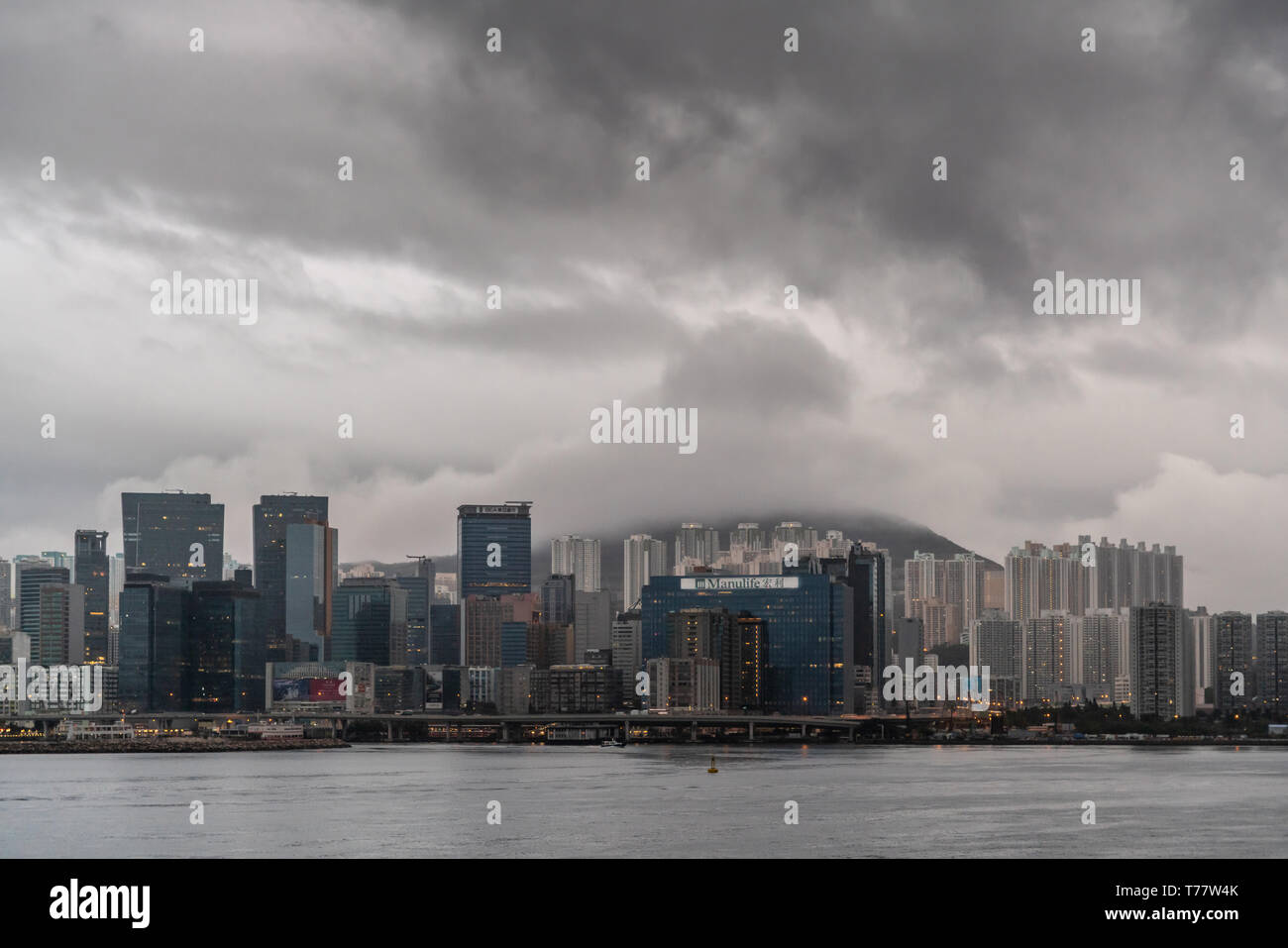 Hong Kong, China - 7. März, 2019: Sehr früh am Morgen unter dunklen regnerischen Himmel. Kowloon Bay, Skyline mit hohen Gebäuden von Kwun Tong Gegend. Manulife Stockfoto