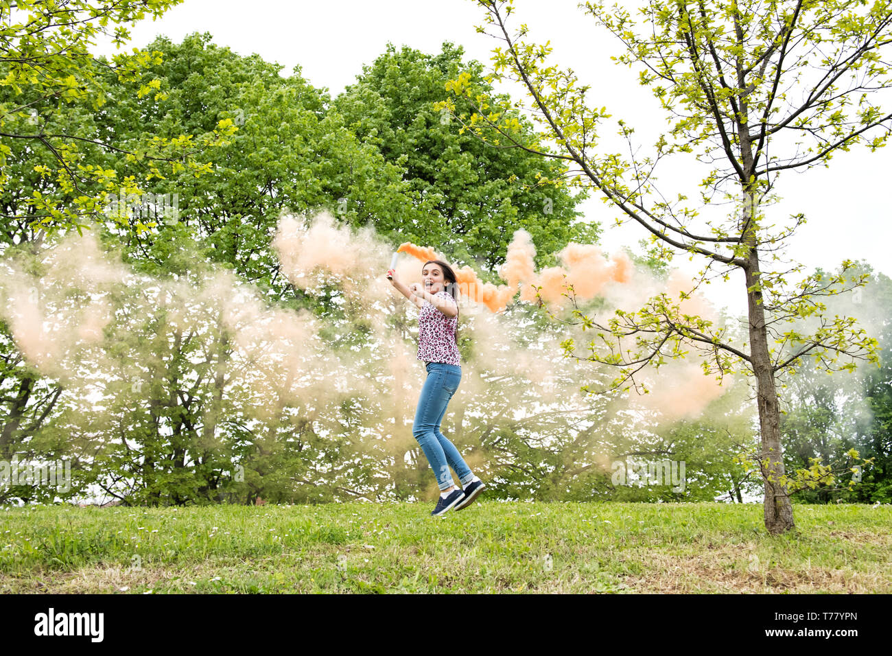 Happy energische junge Mädchen mit einem Rauch flare Laufen und Springen in einem Garten Lachen mit Aufregung Stockfoto