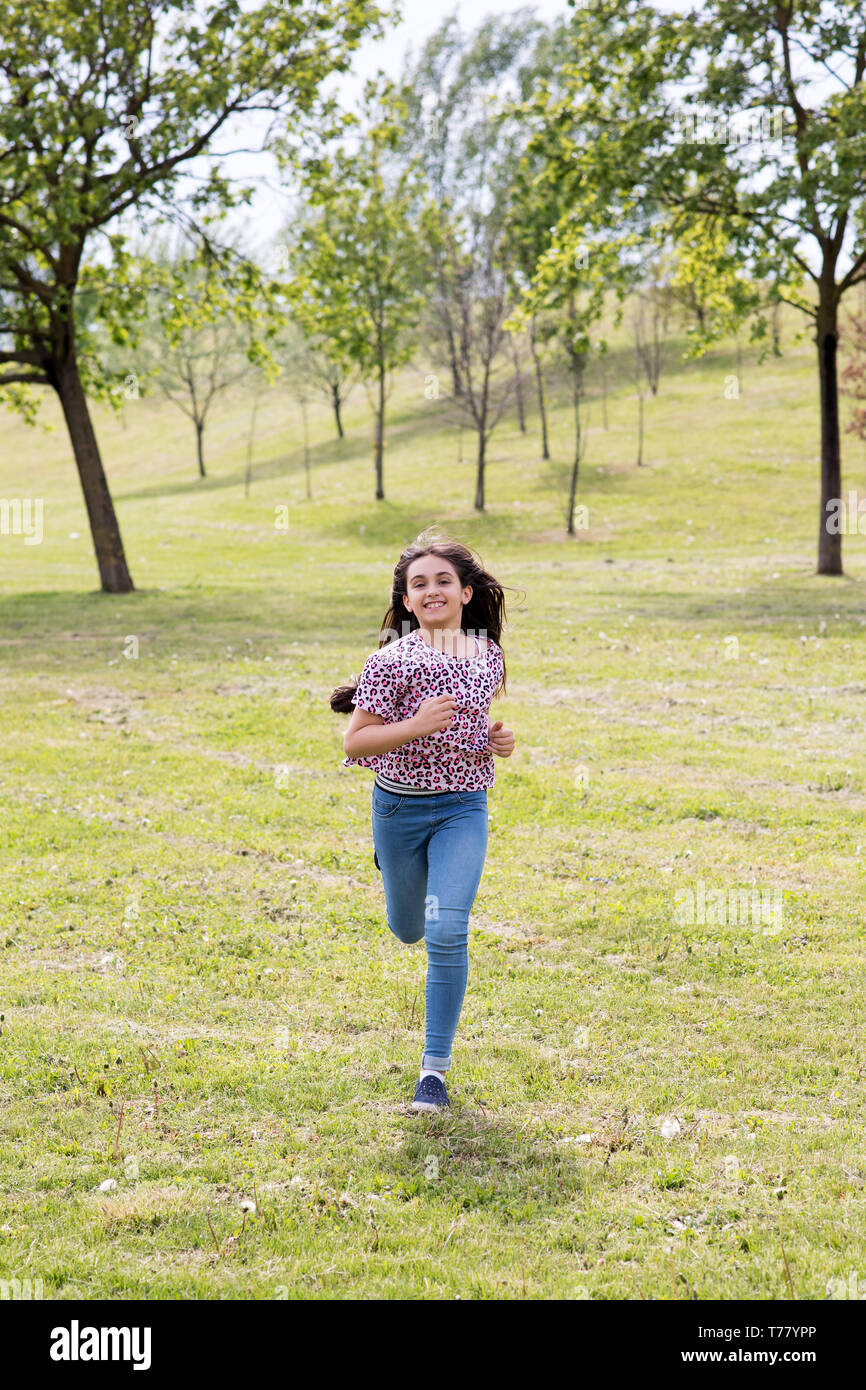 Fit athletische junge Mädchen in Jeans und Turnschuhen durch einen Park im Frühling Sonnenschein mit einem glücklichen Lächeln nähert sich die Kamera Stockfoto