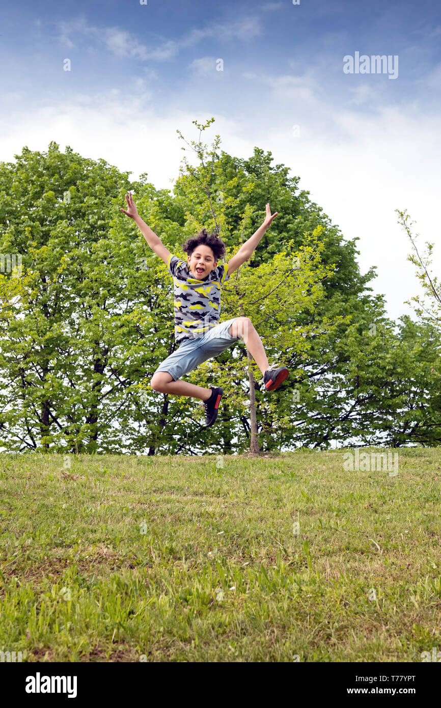 Agile Junge sprang hoch in die Luft, als er über das grüne Gras in einem Park oder Garten seine Feder Freiheit feiern läuft Stockfoto