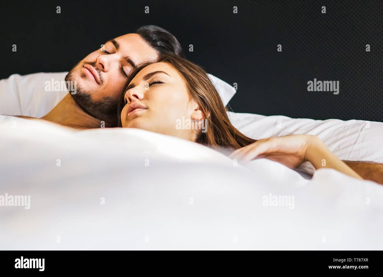 Liebevolle junge Paare schlafen zusammen in einem Bett mit weißen Laken zu Hause - Momente des Lebens von Menschen in Liebe im Schlafzimmer Stockfoto