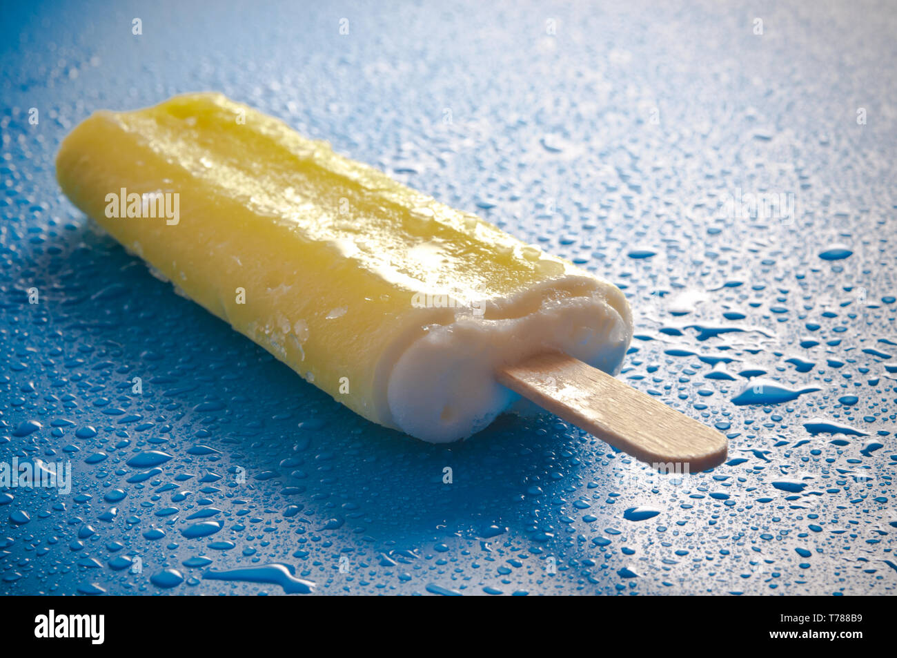 Gelbe Eis am Stiel oder Eis pop auf einem blauen Hintergrund mit Wassertropfen Stockfoto