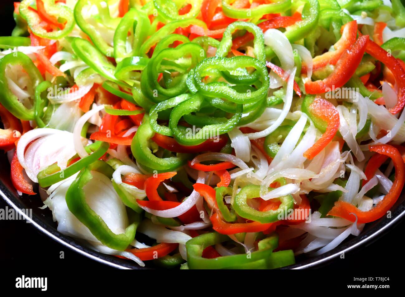 Frisch geschnittene rohe grüne und rote Paprika mit Zwiebel auf Platte Stockfoto