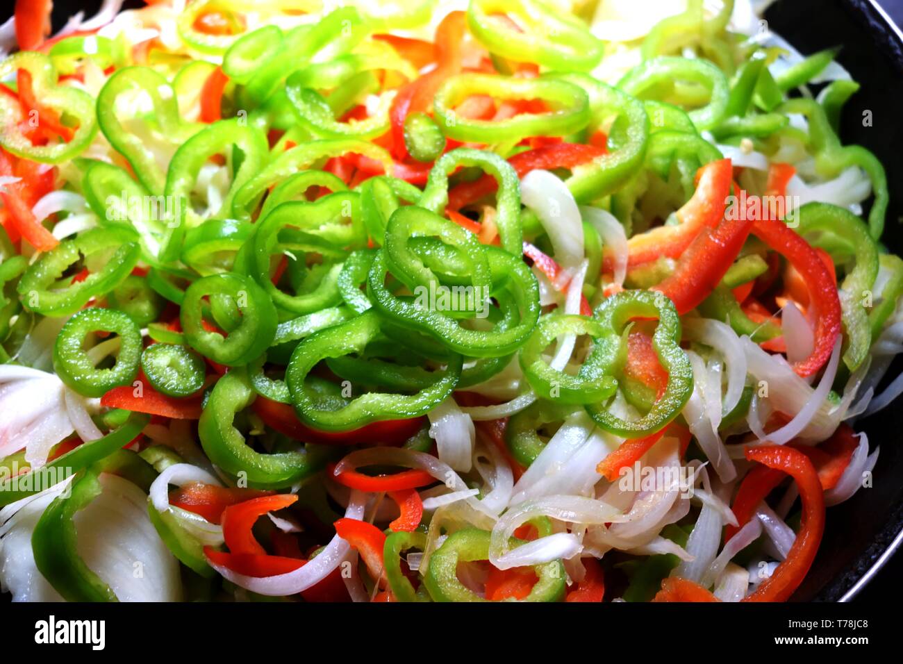 Frisch geschnittene rohe grüne und rote Paprika mit Zwiebel in der Pfanne Stockfoto