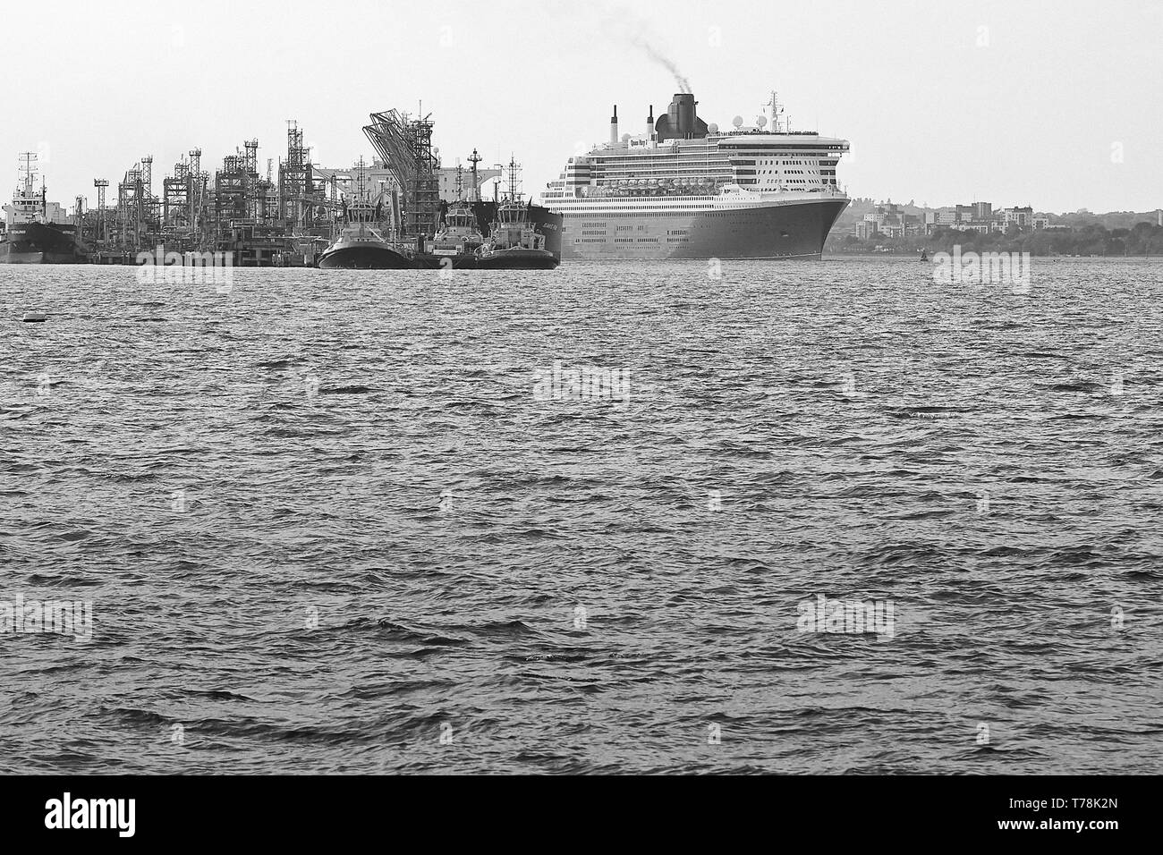 Schwarz-weiß-Foto des Flaggschiffs der Cunard-Linie, RMS QUEEN MARY 2, der an der Fawley Oil Refinery vorbeidampft, als sie Southampton nach New York verlässt Stockfoto