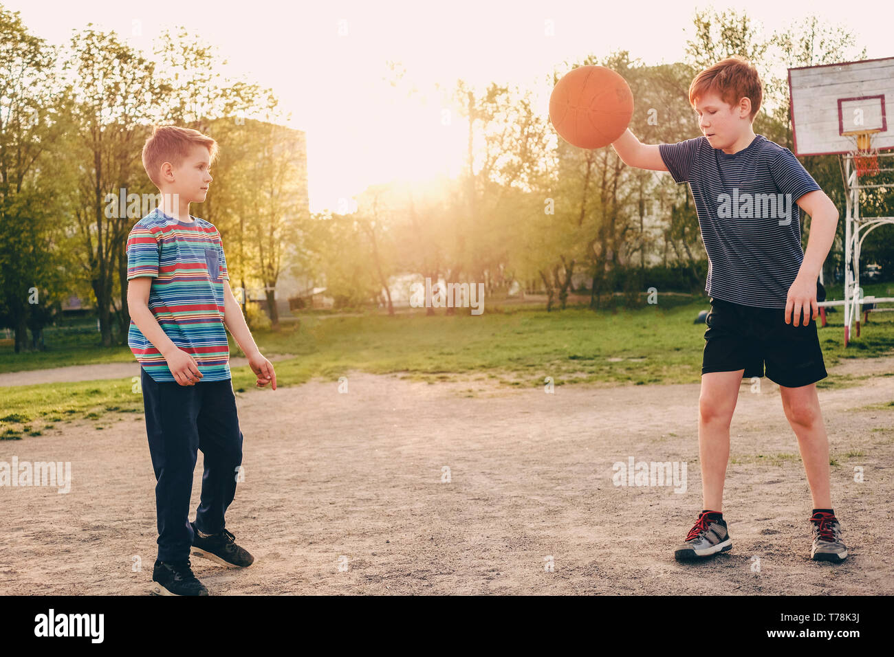 Zwei Jungen üben ihre Basketball Skills im warmen Abendlicht auf einen Sportplatz mit einem Springen der Defensive bewegt sich der Zweite zu vermeiden. Stockfoto