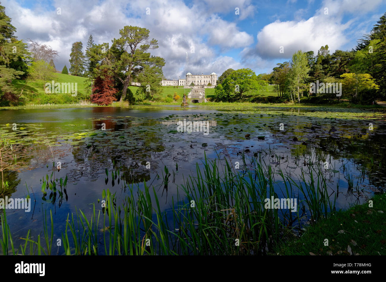 Blick über den See und die Gärten auf der sonnenbeschienenen Powerscourt House, Irland, mit einem Spiegelbild im Wasser zwischen dem Wasser Lily Pads Stockfoto