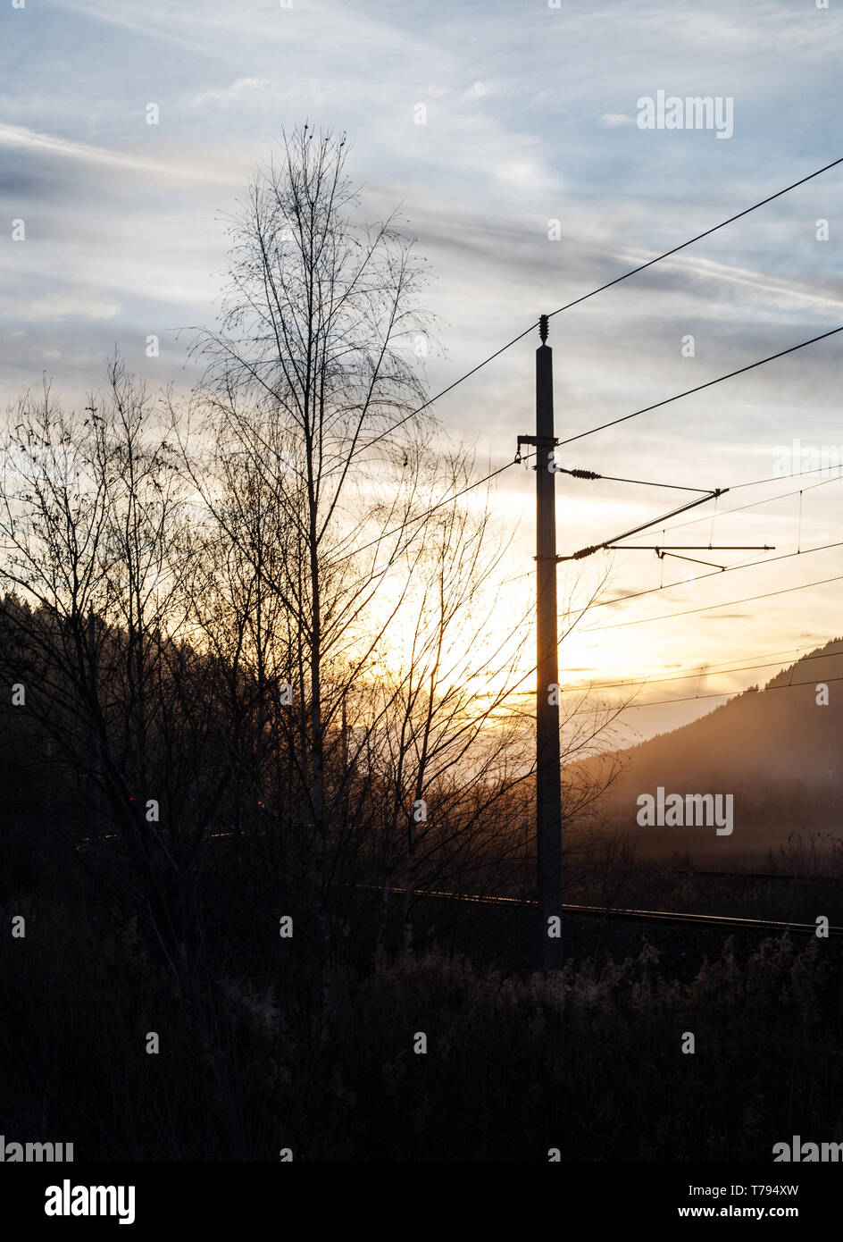 Sonnenuntergang in einer nebligen mystische Landschaft mit kleinen Büschen und Schienen mit Stromleitungen in der Steiermark Stockfoto