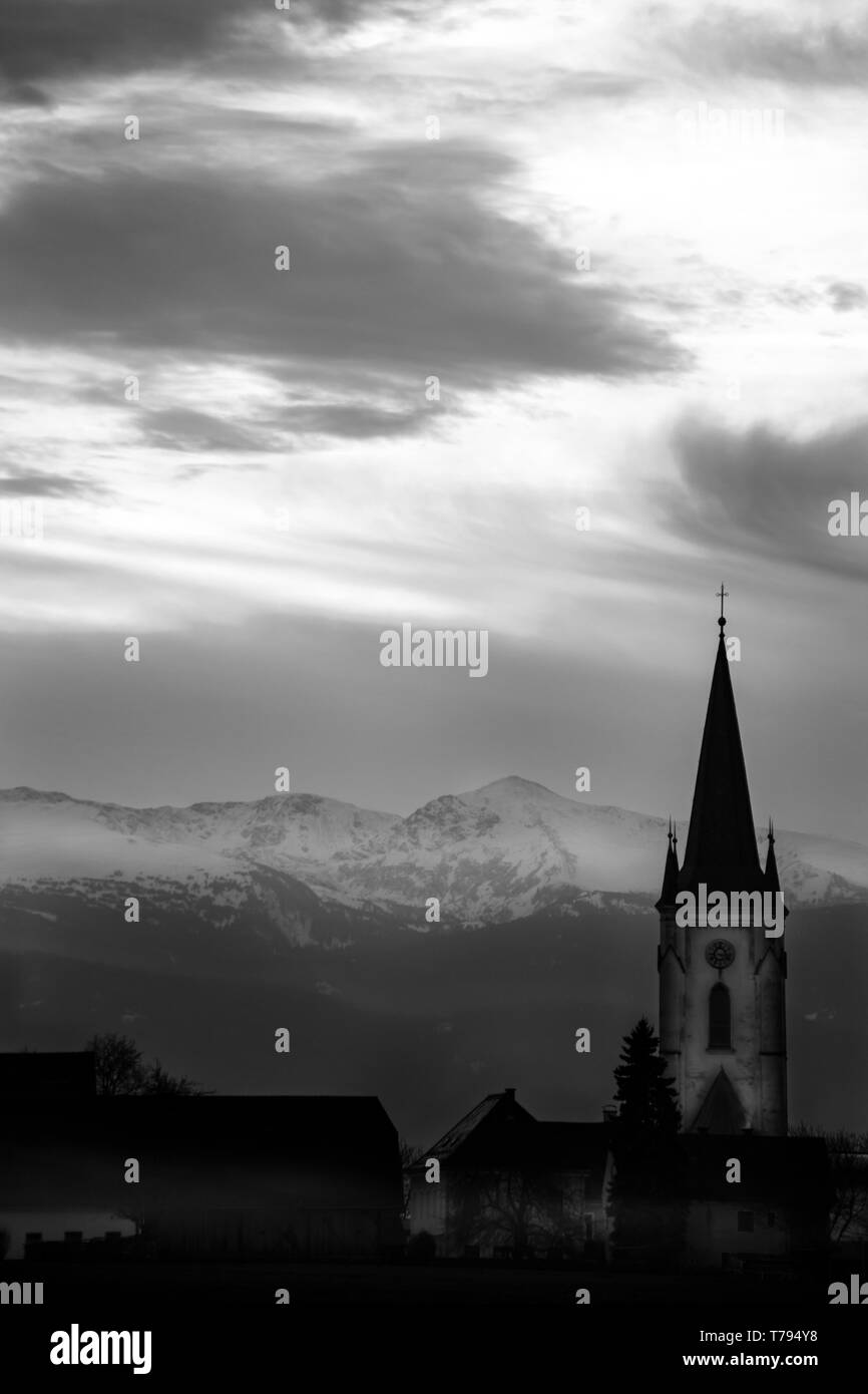 Sonnenuntergang in einer nebligen mystische Landschaft mit Wolken und ein Berg Silhouette mit Kirchturm in den österreichischen Alpen Stockfoto