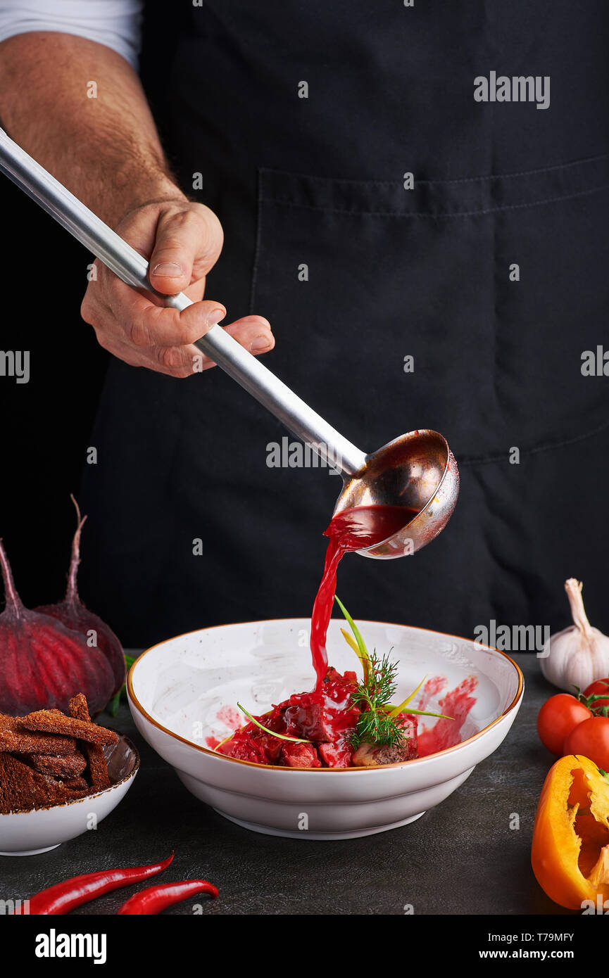 Küchenchef gießt rote Suppe borschtsch von Kelle. Ukrainische und russische Küche Konzept. Vertikale. Platz kopieren Stockfoto