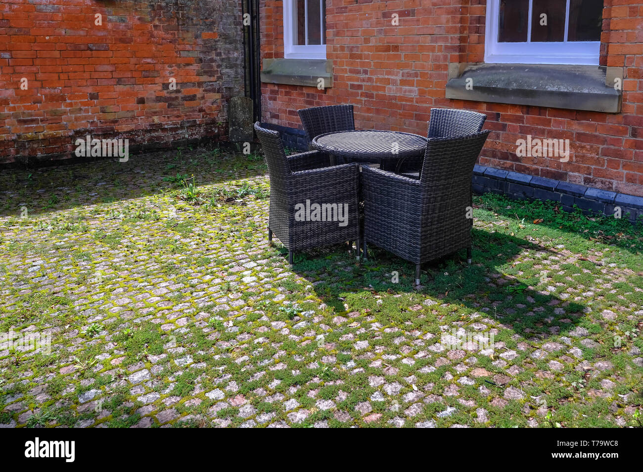 Rattan Tisch und Sesseln in dunklem Grau in einem alten Innenhof mit einem roten Hintergrund. Unkraut und Moos zwischen die Pflastersteine Hinzufügen einem traditioana Stockfoto