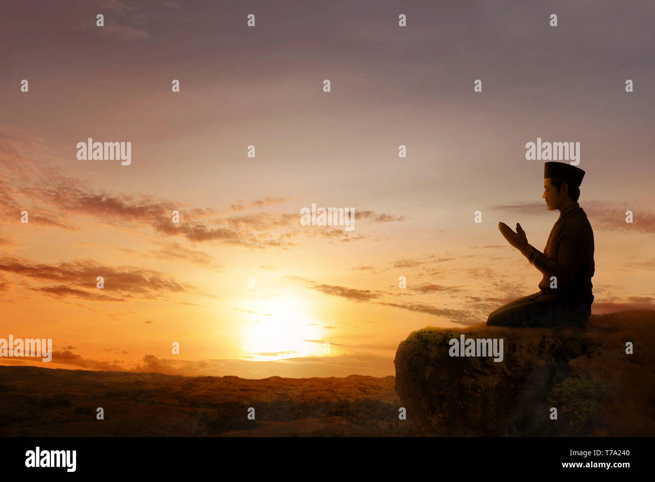 Asiatische muslimischen Mann in beten Position sitzen, während erhobenen Hände und betend auf dem Rand der Klippe mit Sonnenuntergang und Landschaften Hintergrund Stockfoto