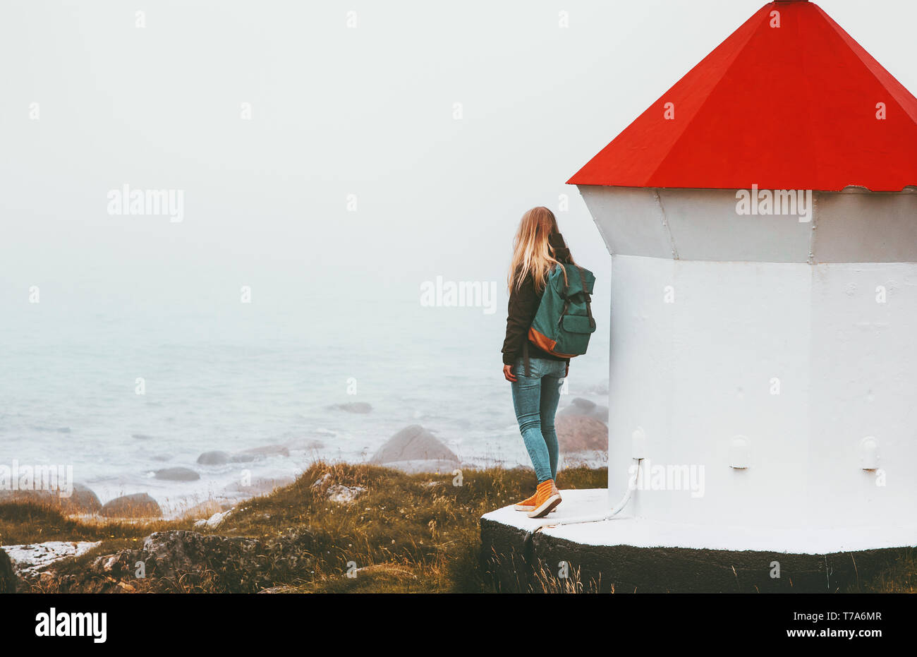 Reisende Frau und Leuchtturm am nebligen Meer solo Reisen lifestyle Abenteuer skandinavischen Reise outdoor Einsamkeit Gefühle Stockfoto
