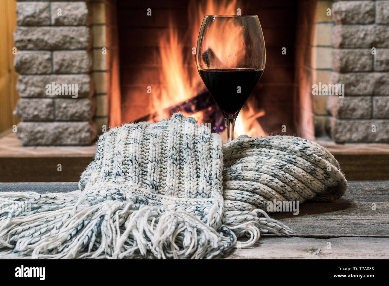 Glas Rotwein und warmer Schal gegen den gemütlichen Kamin Hintergrund, in Country House, horizontal, hygge, Home sweet home. Stockfoto