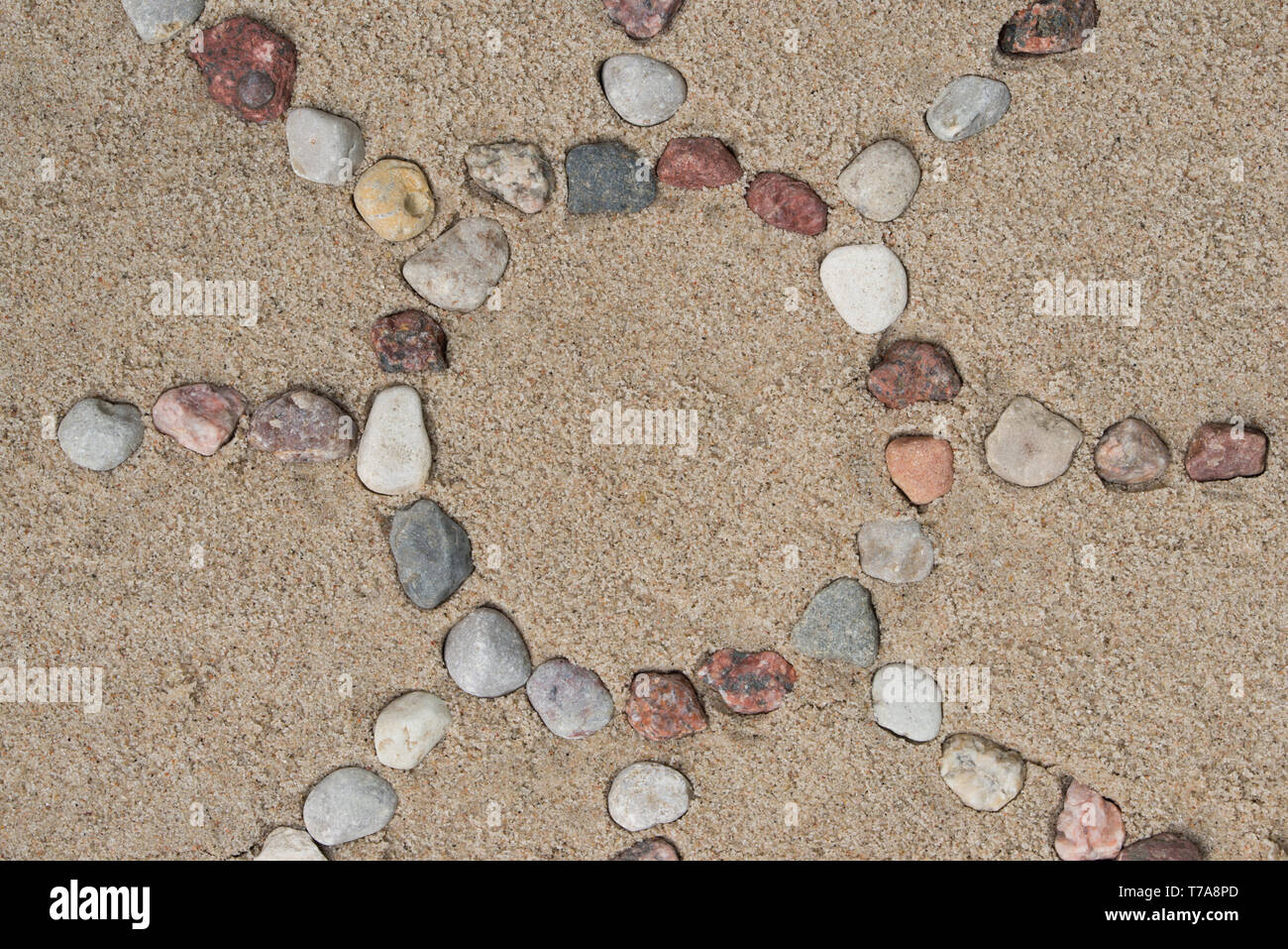 Sun Form aus Kieselsteinen auf Sand Hintergrund Textur Stockfoto