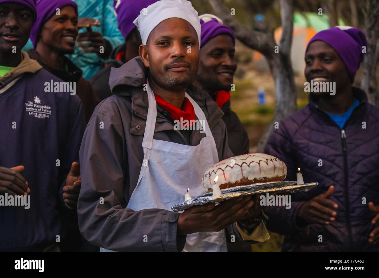 Afrikanische Menschen, um meinen Geburtstag zu feiern, in einem Dschungel versammelt, glückliche Männer singen Lieder und Spaß im Freien. Tragen warme Jacken und Mützen. Mann Stockfoto