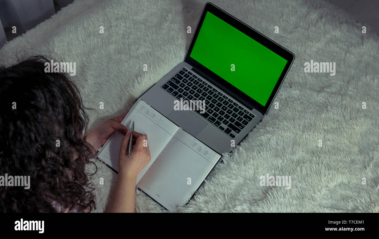 Die junge Frau über ein Laptop zu Hause bei einer Tasse Tee in der Hand. Der Laptop mit Green Screen Stockfoto